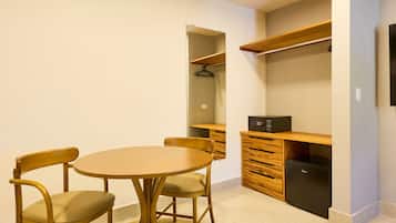 Een compacte kamer met een ronde tafel, twee stoelen, een houten kast, een kleine zwarte koelkast en een kapstok.