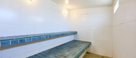 A bathroom with white tiled walls, a blue-tiled bench, and two wall-mounted lights.
