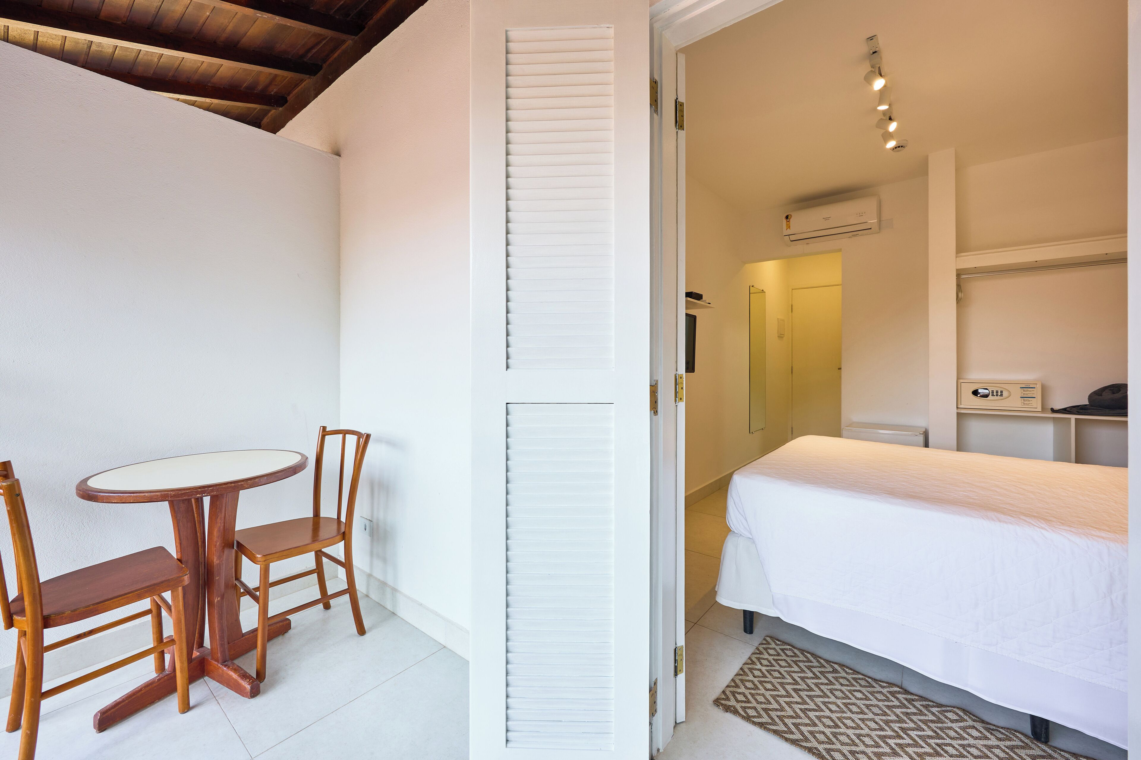 Une chambre à coucher avec un lit, une petite table, deux chaises et un mur blanc avec une fenêtre.