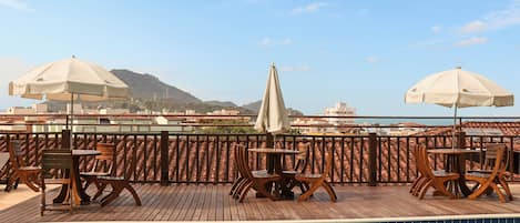 Zona de piscina en la azotea con terraza de madera, barandillas metálicas y dos sombrillas con la etiqueta 'Hotel Capelle'.