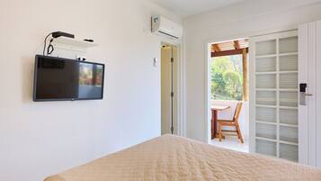 A bedroom with a bed, a TV mounted on the wall, an air conditioning unit, and a sliding door leading to an outdoor area with a table and chair.