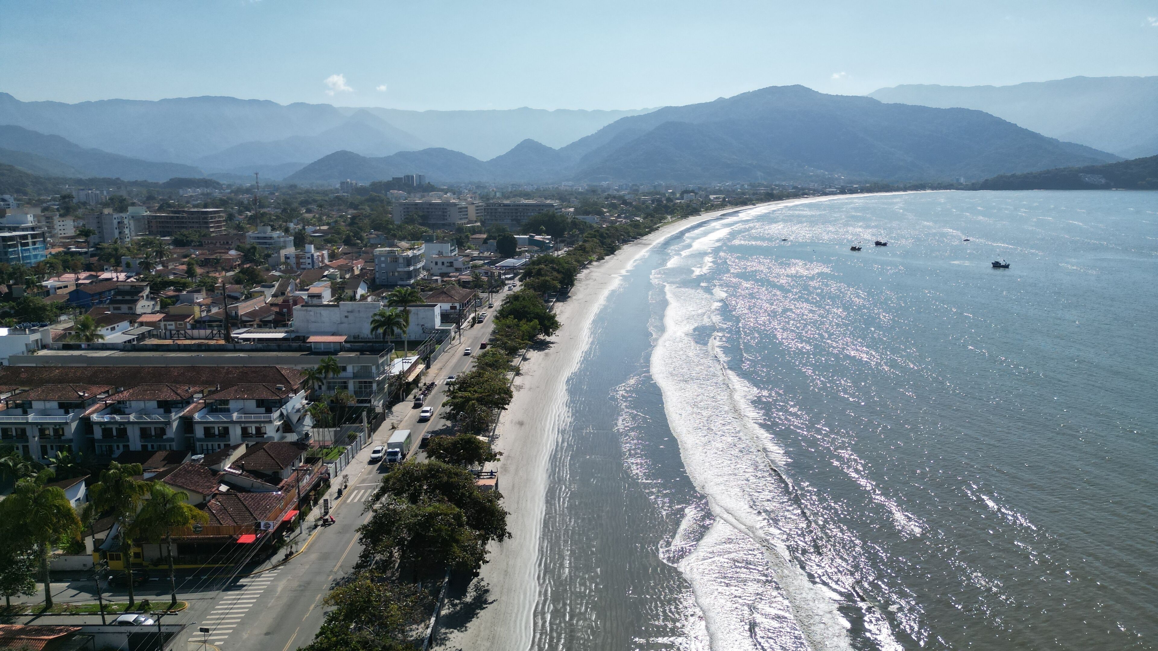 A coastal city with a long beachfront, buildings along the shore, and mountains in the background.