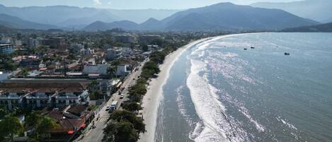 A coastal city with a long beachfront, buildings along the shore, and mountains in the background.