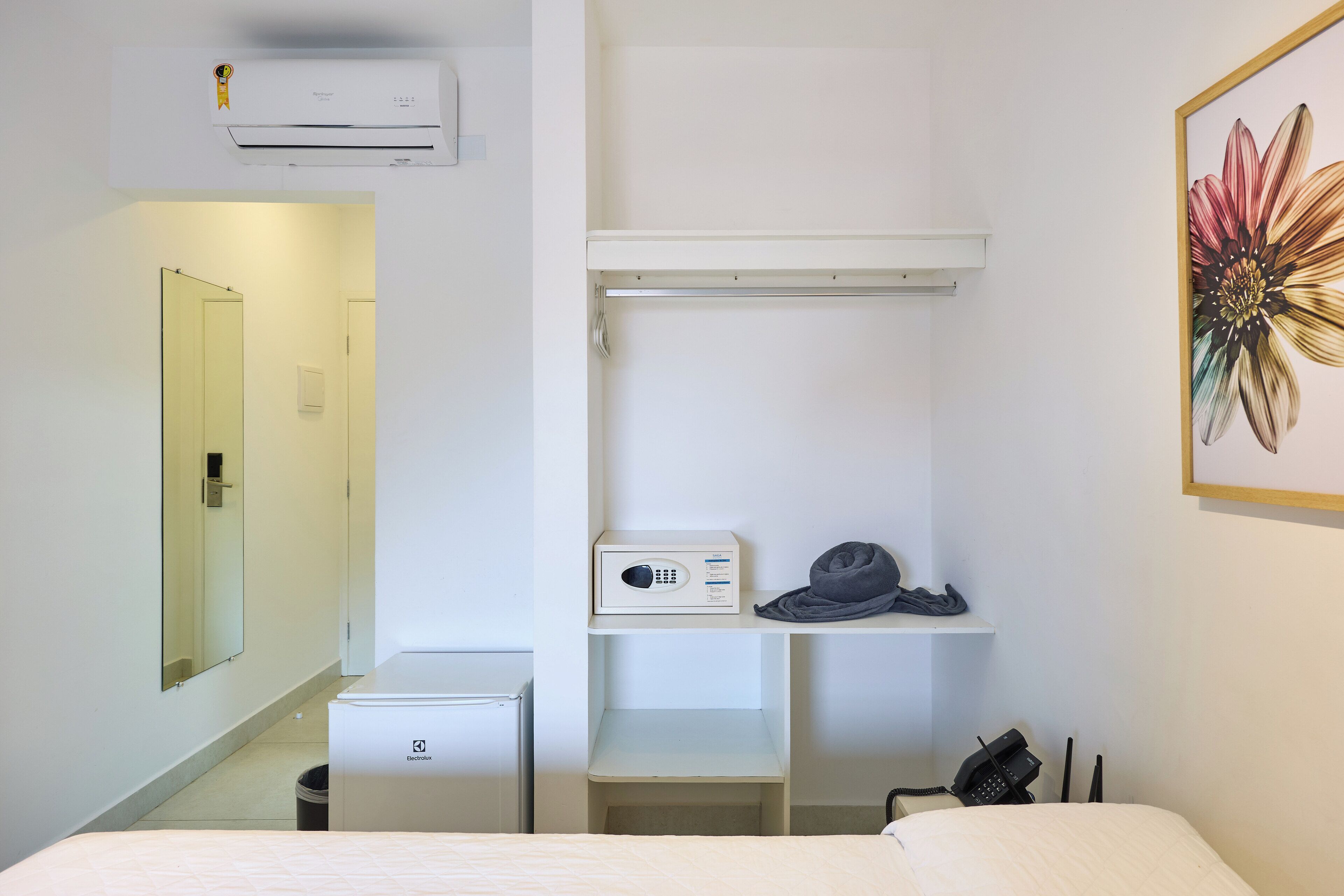 A hotel room with a bed, a small desk, a microwave, a trash bin, and a wall-mounted air conditioner.