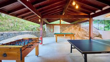Un espace de loisirs intérieur comprenant une table de baby-foot, une table de ping-pong et une table de billard.