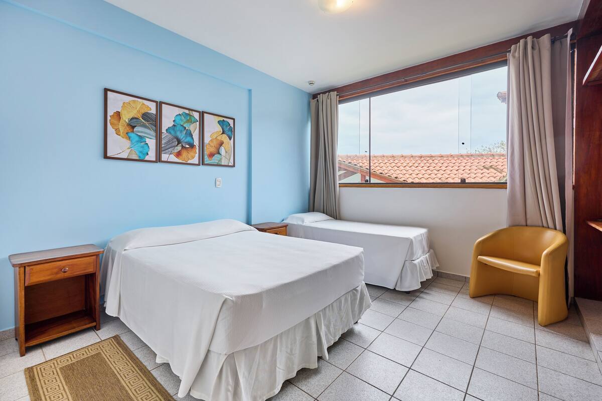 A hotel room with two beds, a wooden nightstand, a chair, and a window with curtains.