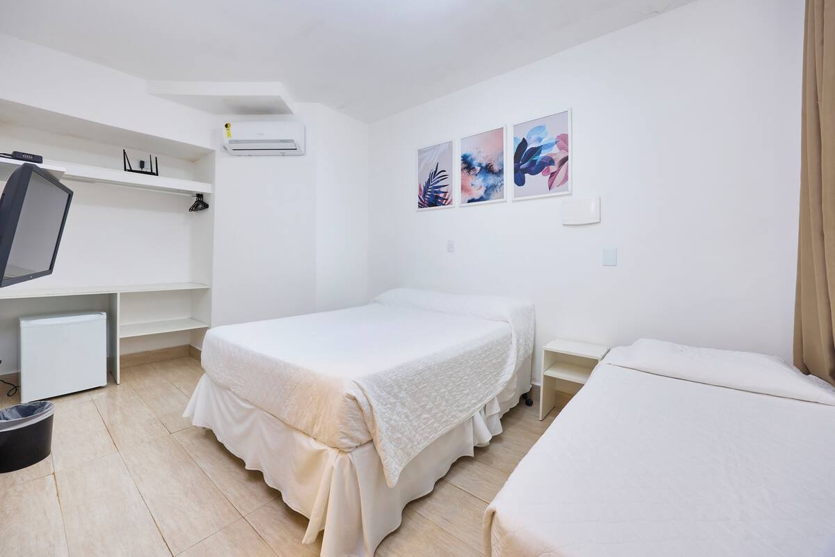 A hotel room with two beds, a TV, a desk, and a shelf.