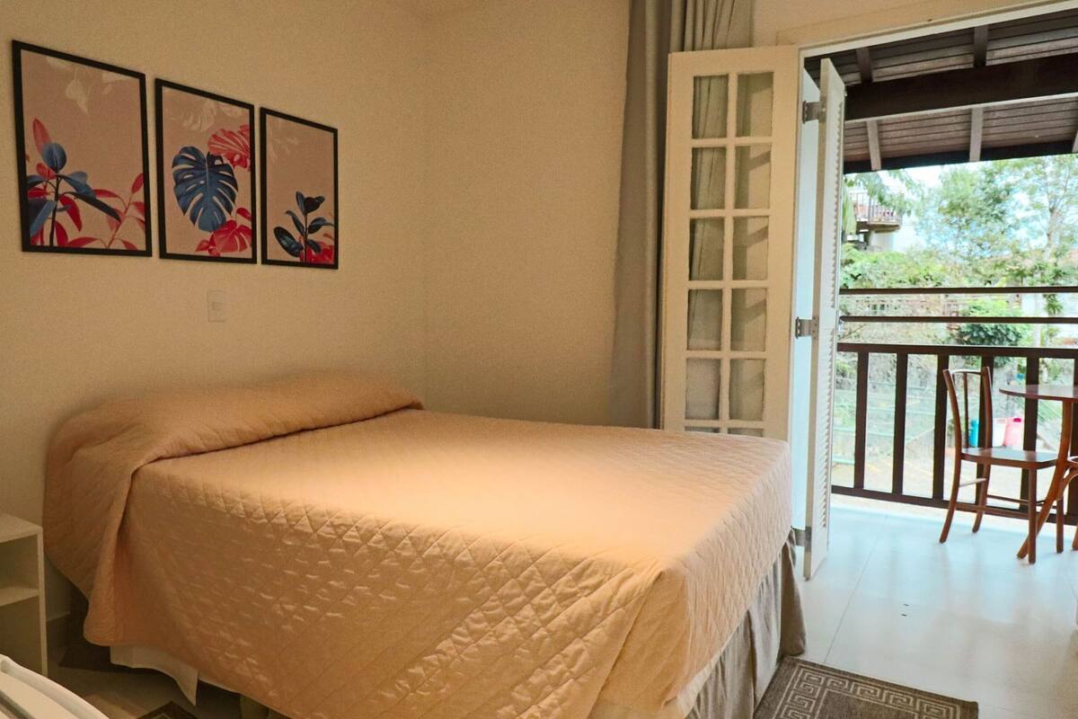 A bedroom with a bed, a small bedside table, and a balcony with chairs.