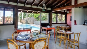 Un restaurant amb taules i cadires de fusta, vista a la piscina i una paret de pedra.