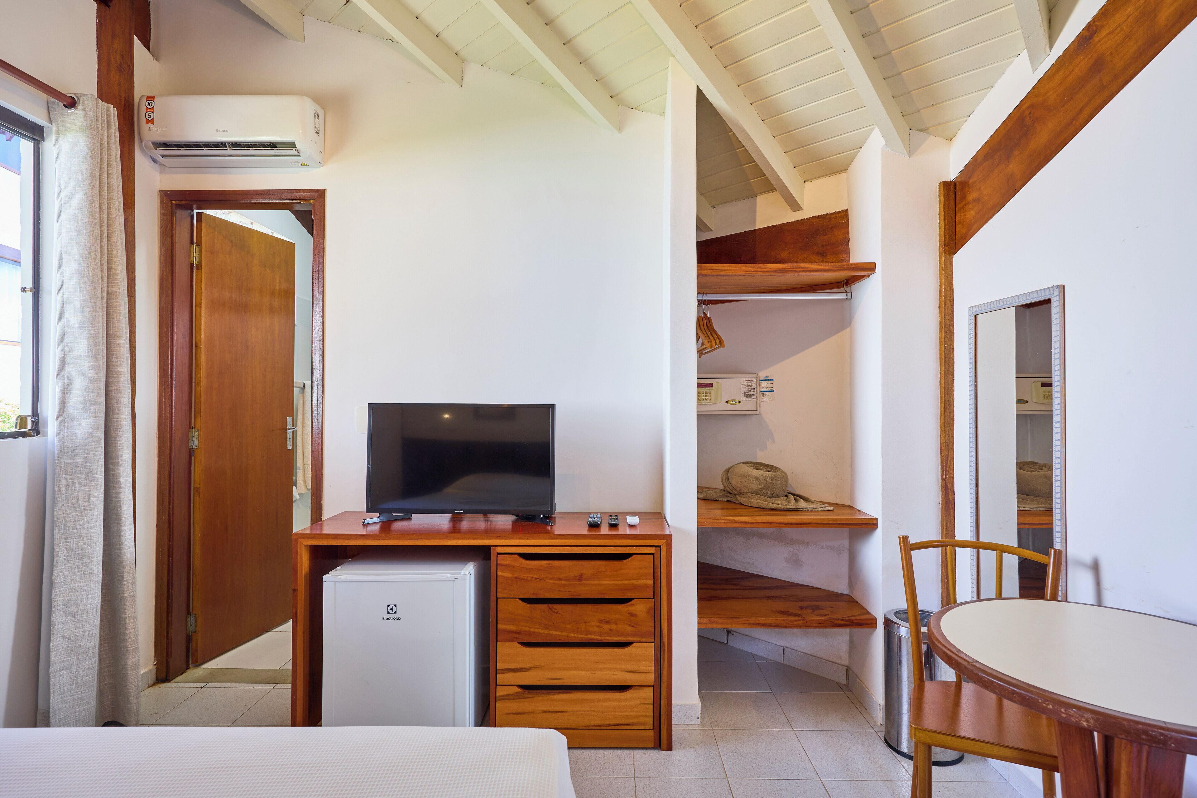 Una habitación de hotel compacta con escritorio de madera, televisor, refrigerador pequeño y mesa de comedor con sillas.
