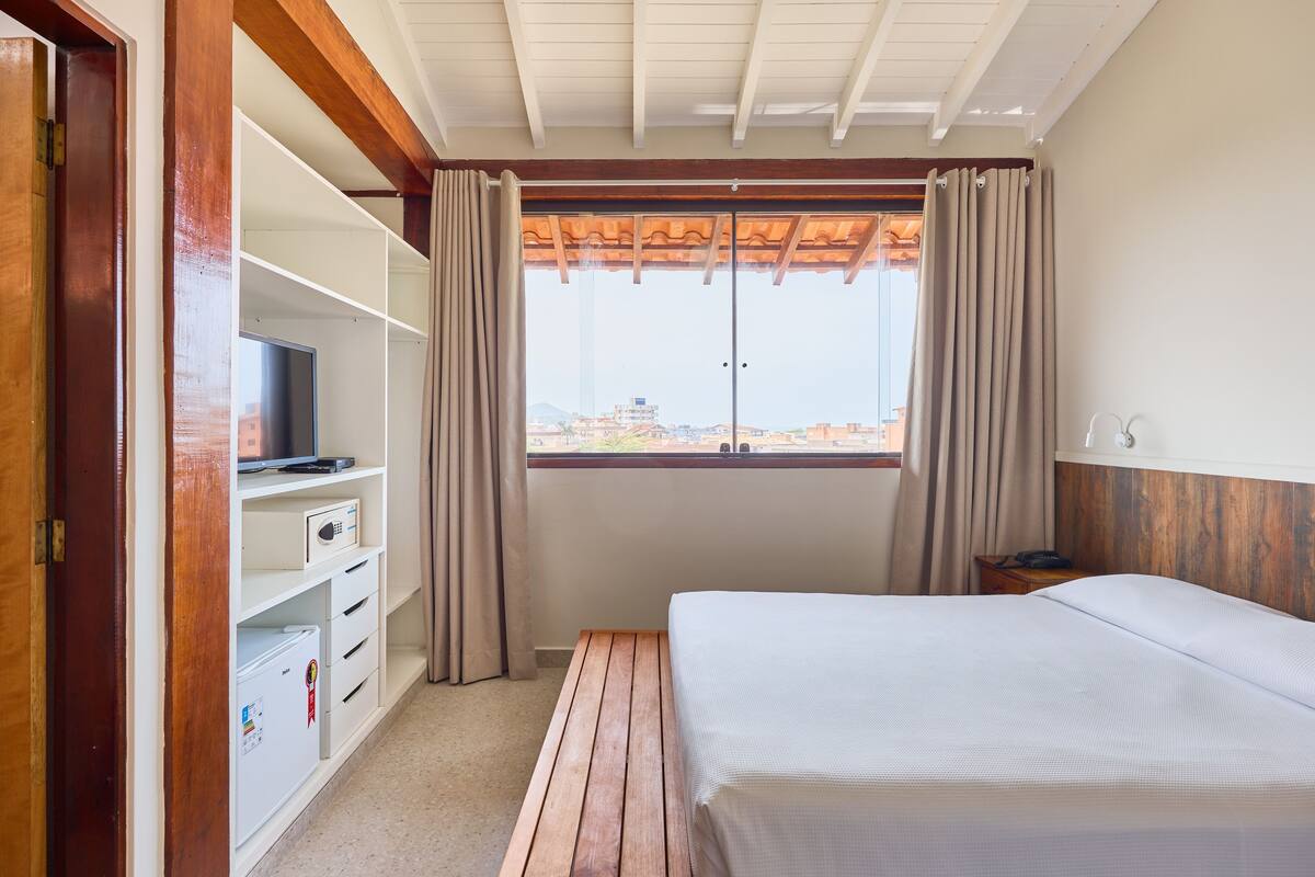 A hotel room with a bed, a TV, a mini-fridge, and a window with curtains.