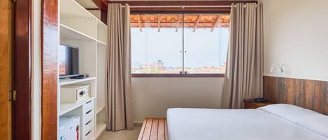 Ein Hotelzimmer mit Bett, Fernseher, Minikühlschrank und einem Fenster mit Vorhängen.