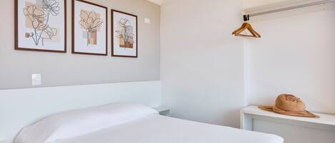 Un dormitorio con una cama, una mesita de noche, un perchero de madera colgante y tres cuadros con motivos florales en la pared.