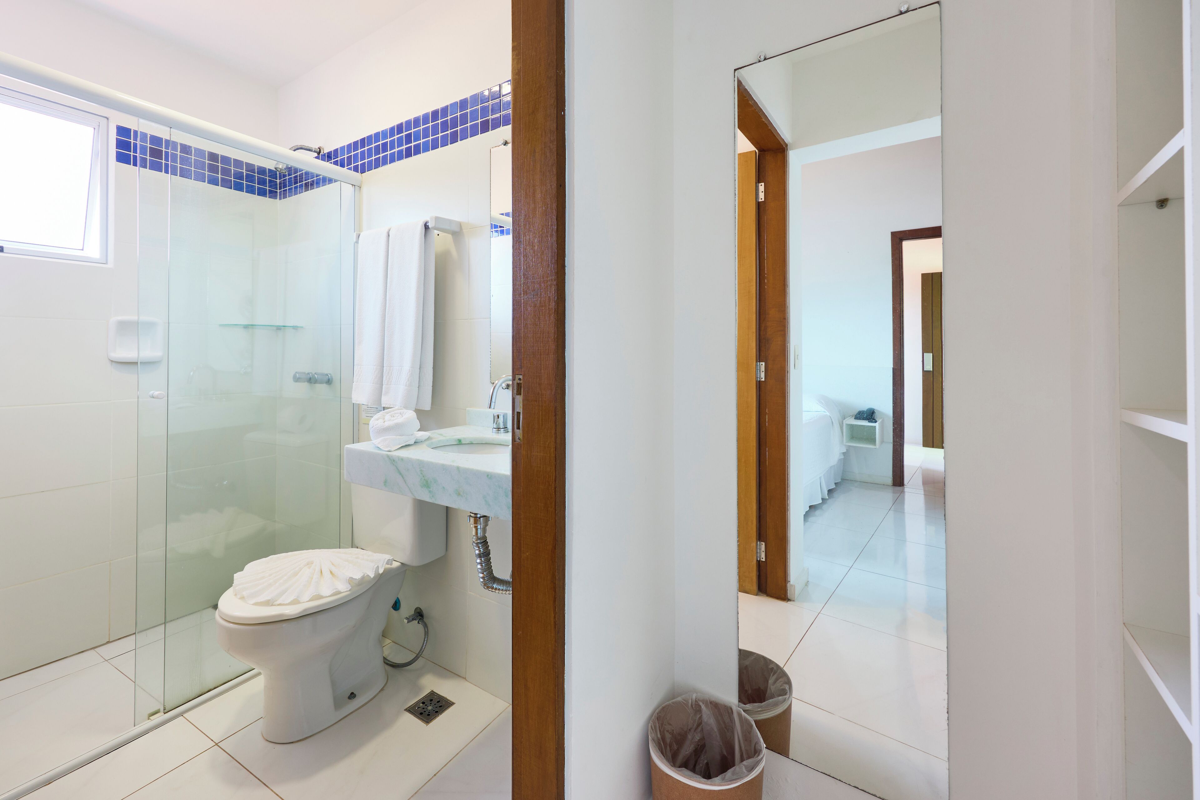 Un baño con cabina de ducha de vidrio, un inodoro, un lavamanos con espejo y un cubo de basura.