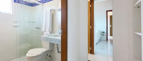 Un baño con cabina de ducha de vidrio, un inodoro, un lavamanos con espejo y un cubo de basura.