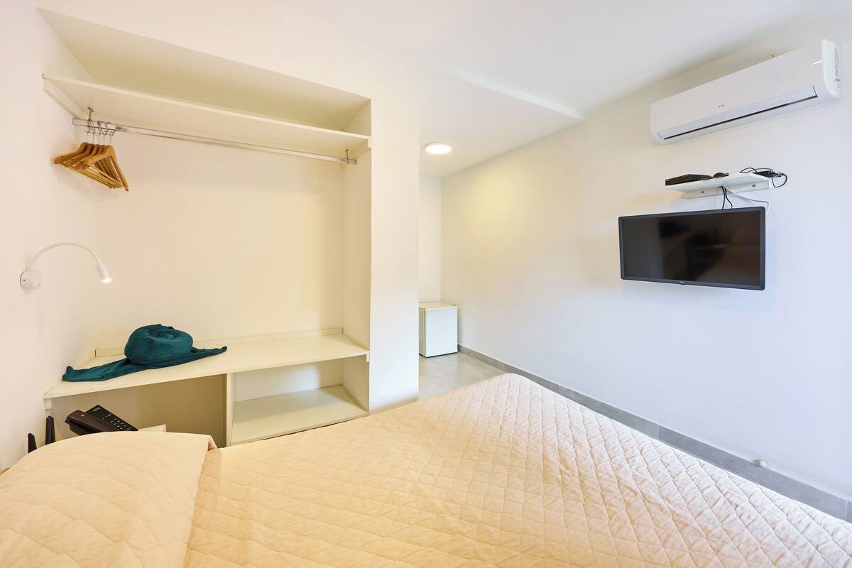 A modern hotel room with a bed, a desk, a TV, and a wardrobe.
