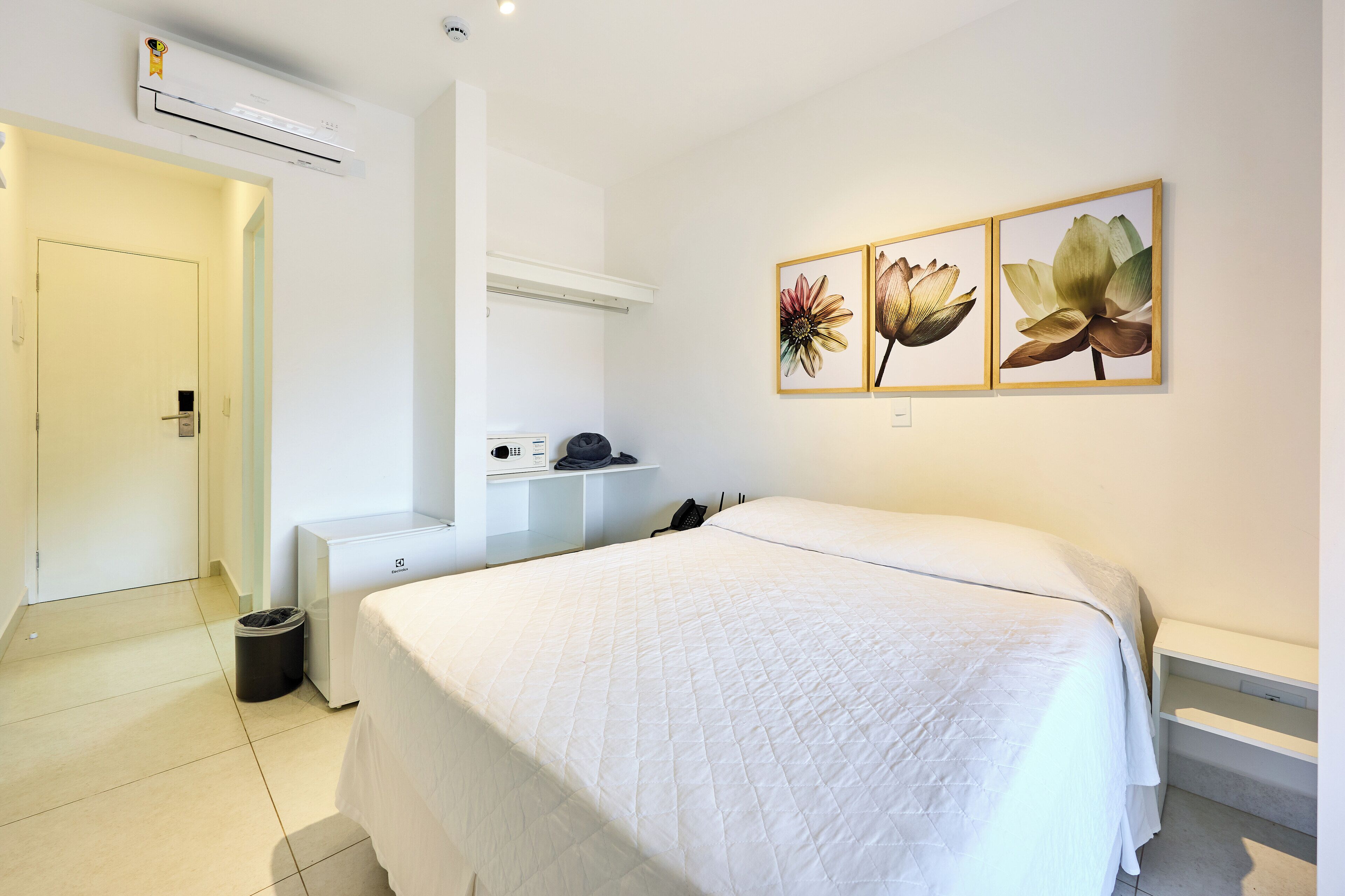 Una habitación de hotel con una cama grande, un escritorio, una silla, aire acondicionado y un cubo de basura.