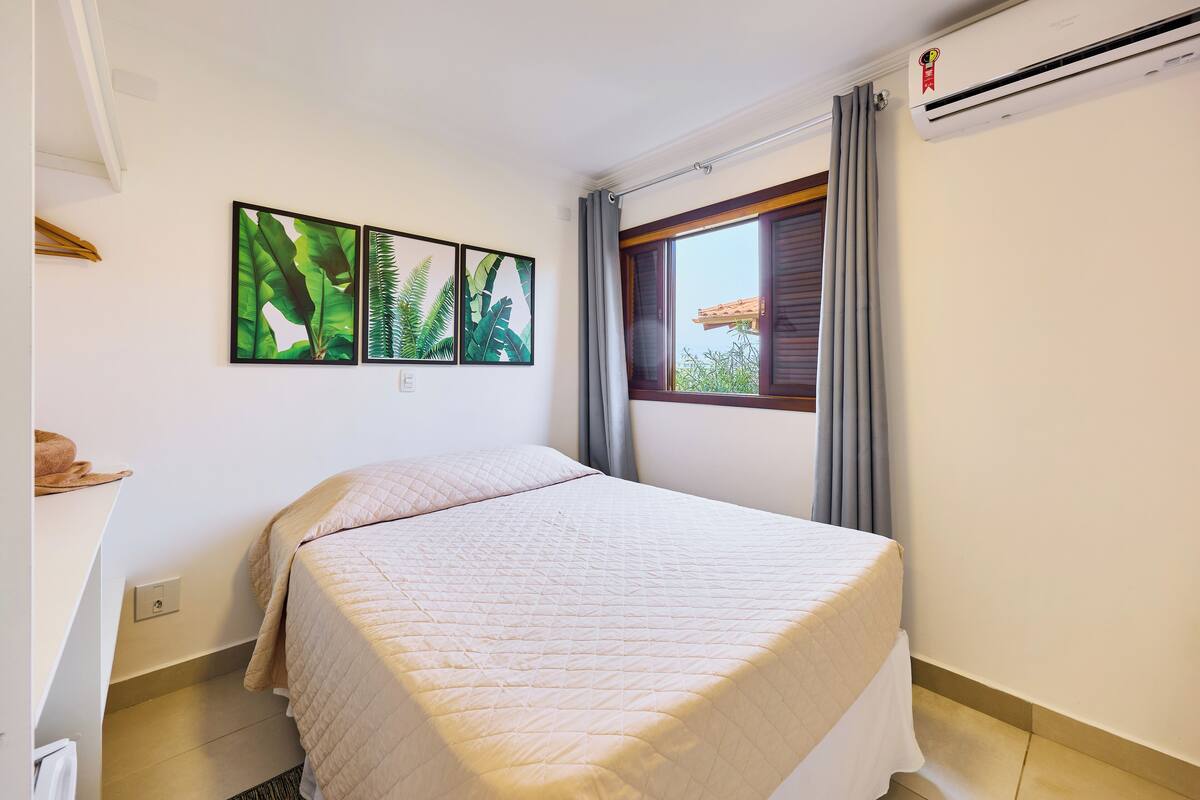 A bedroom with a bed, a window with curtains, and three framed pictures on the wall.