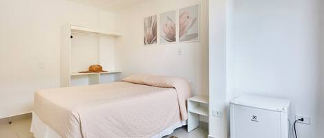 Une chambre comprenant un lit, une petite armoire blanche, une étagère fixée au mur et un réfrigérateur compact.