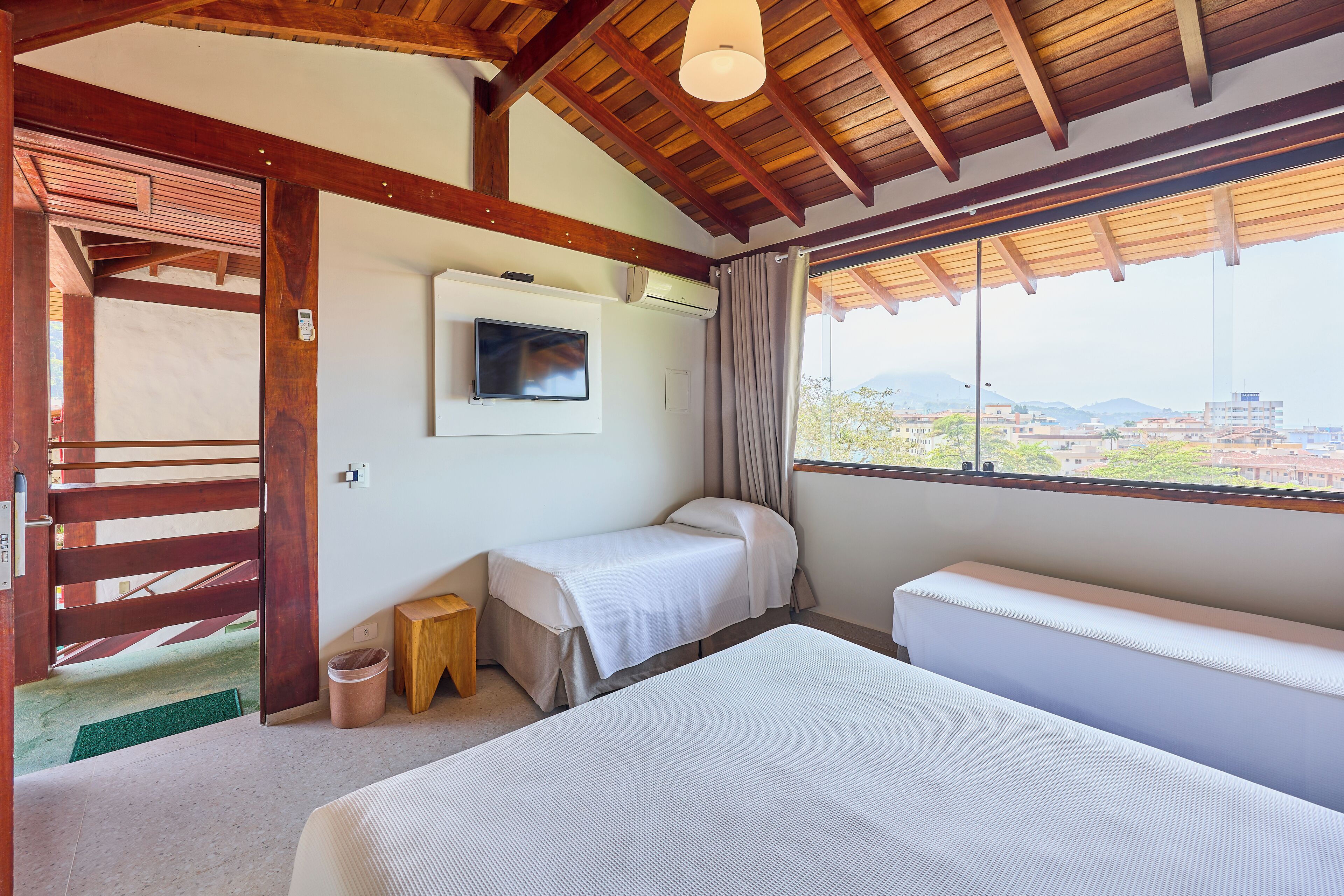 A bedroom with a bed, a bench, a TV, and a window with a view.