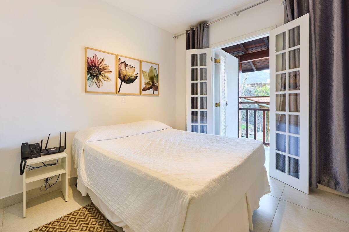 A bedroom with a bed, a nightstand, a door to an outdoor area, and a wall with three framed pictures.