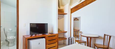 Un dormitorio con una cama, un televisor sobre un escritorio de madera, un refrigerador pequeño, un espejo y una silla.