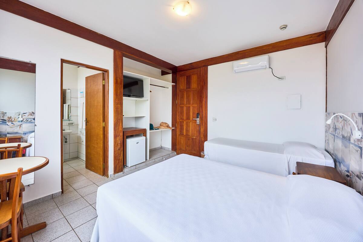 A hotel room with a bed, a desk, and a chair. There is a wooden door leading to a bathroom and a kitchenette.