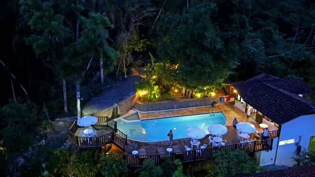 Una piscina exterior envoltada per un pont de fusta i seients de relax, amb vista a un bosc dens al fons.