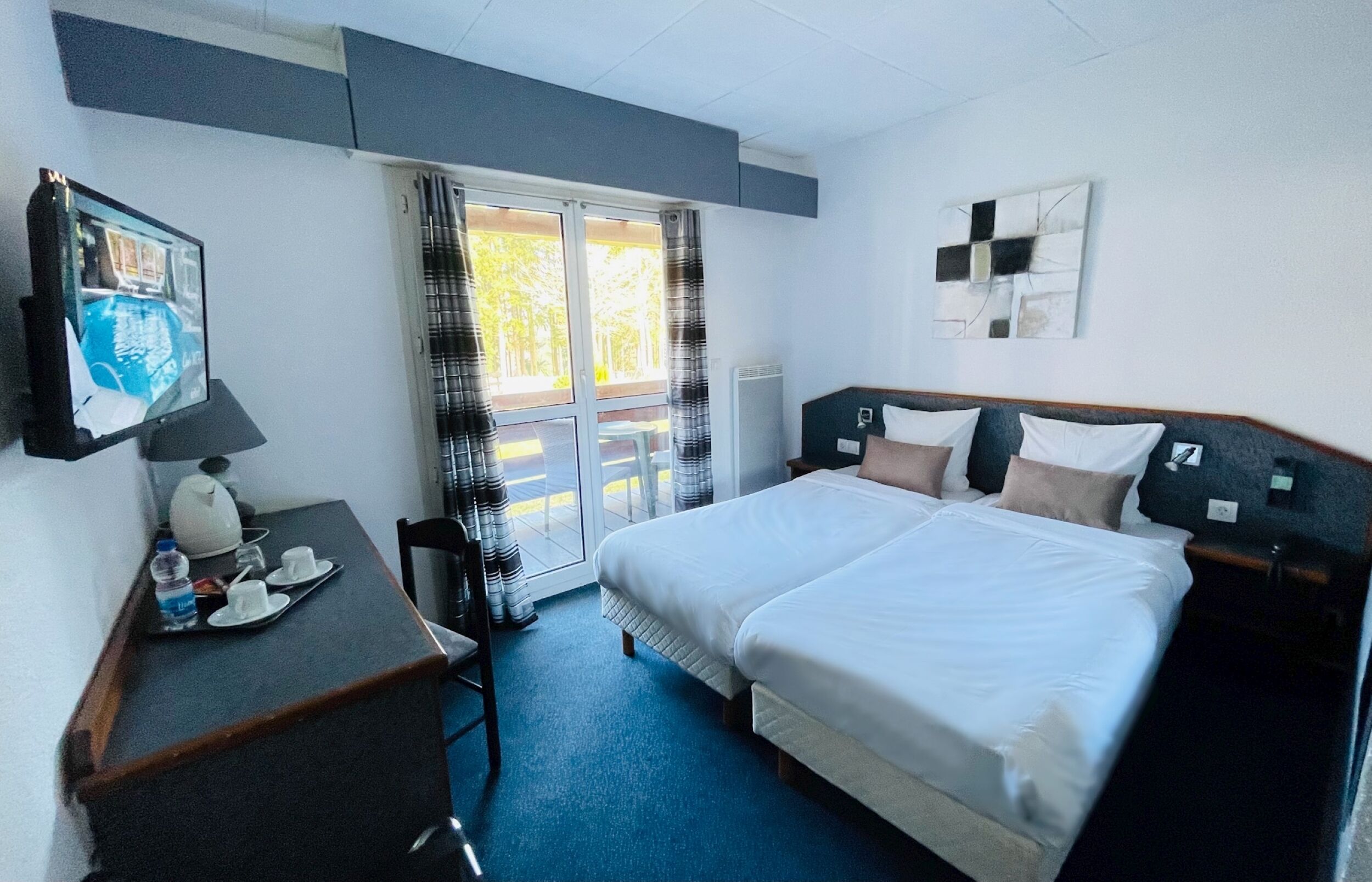 Ein Hotelzimmer mit einem Bett, einem Schreibtisch mit Stuhl, einem Fernseher und einem Fenster mit Vorhängen.