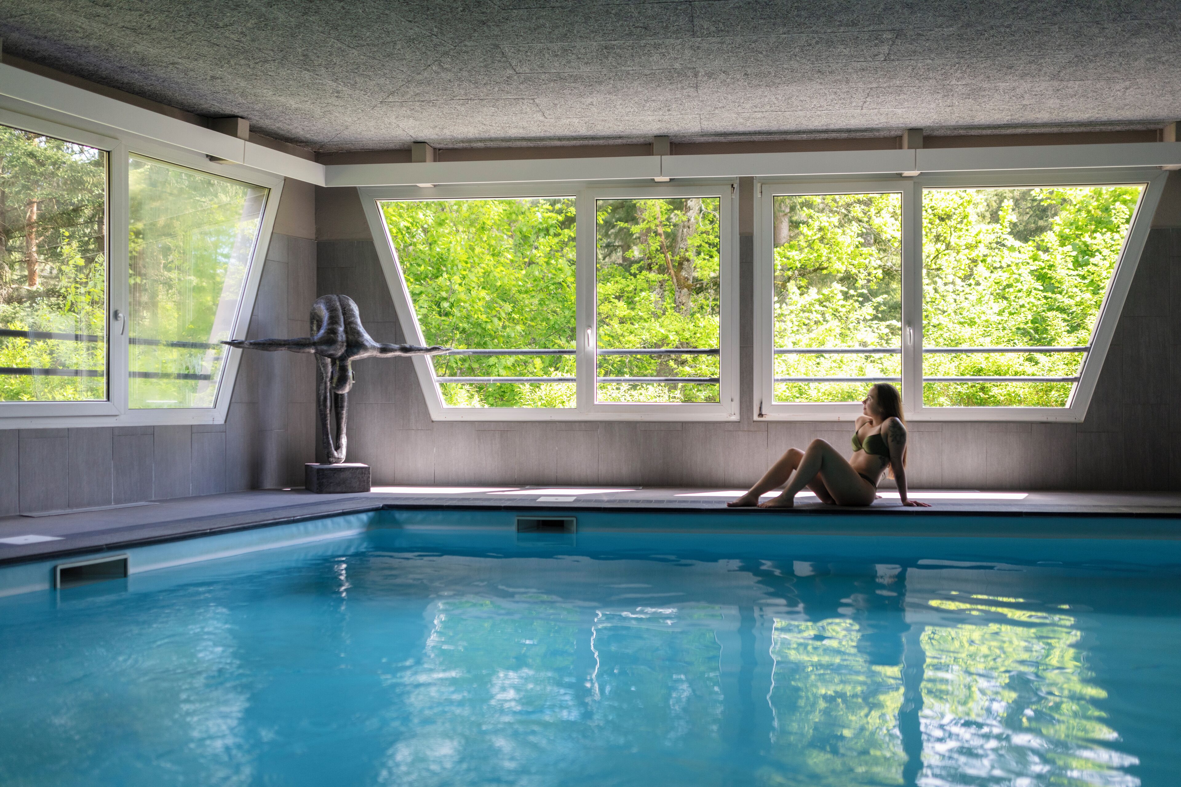 Une piscine intérieure dotée de grandes baies vitrées et ornée d’une sculpture.