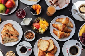 Ein reichhaltiges Frühstücksbuffet mit Croissants, Toast, Früchten und Getränken auf einem Tisch.