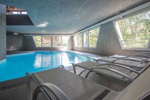 Ein Hallenbad mit freiem Blick durch große Fenster, einer geneigten Decke und sonnendurchfluteten Bereichen.