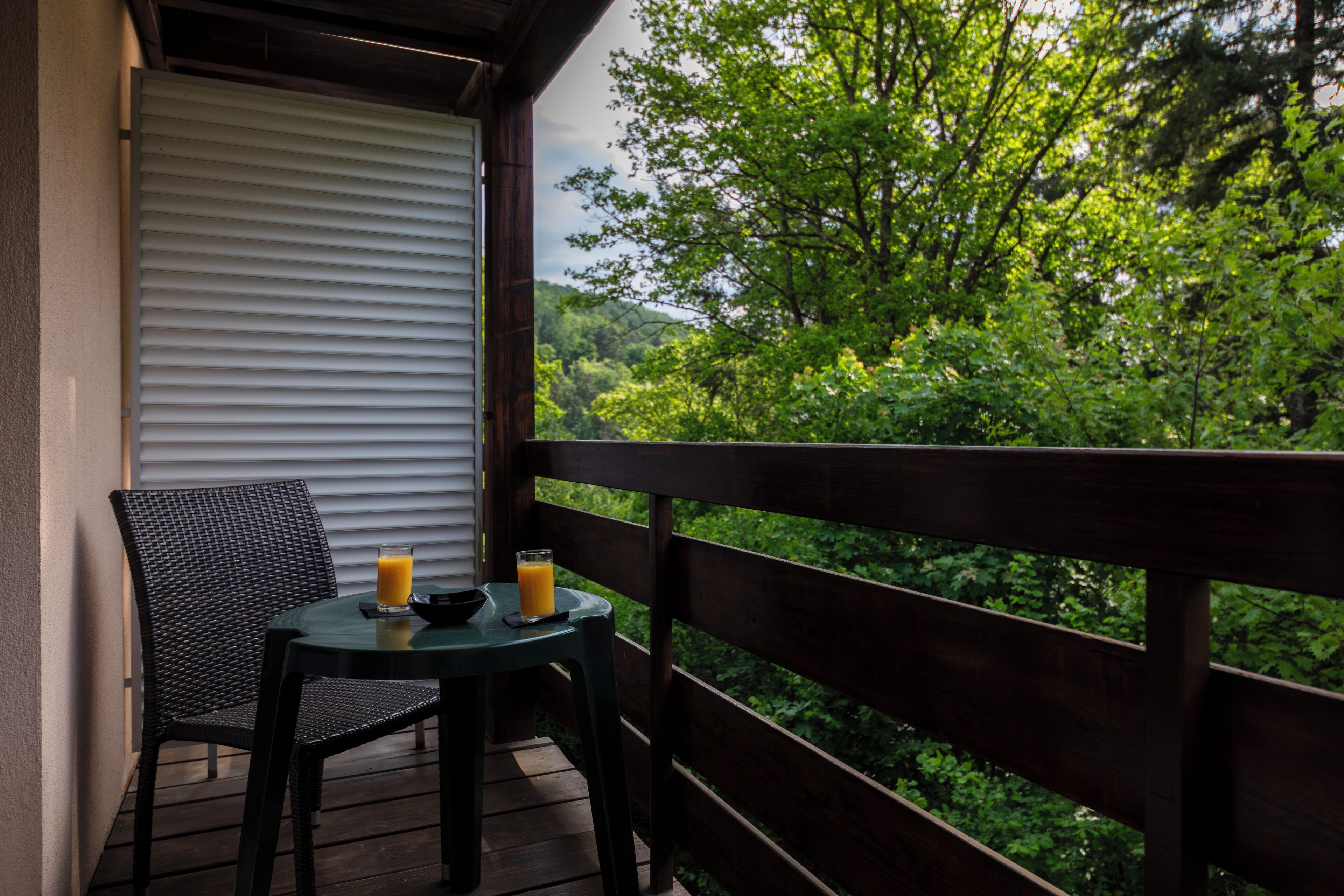 A balcony with a wooden railing, a wicker chair, and a small table with two glasses of orange juice.