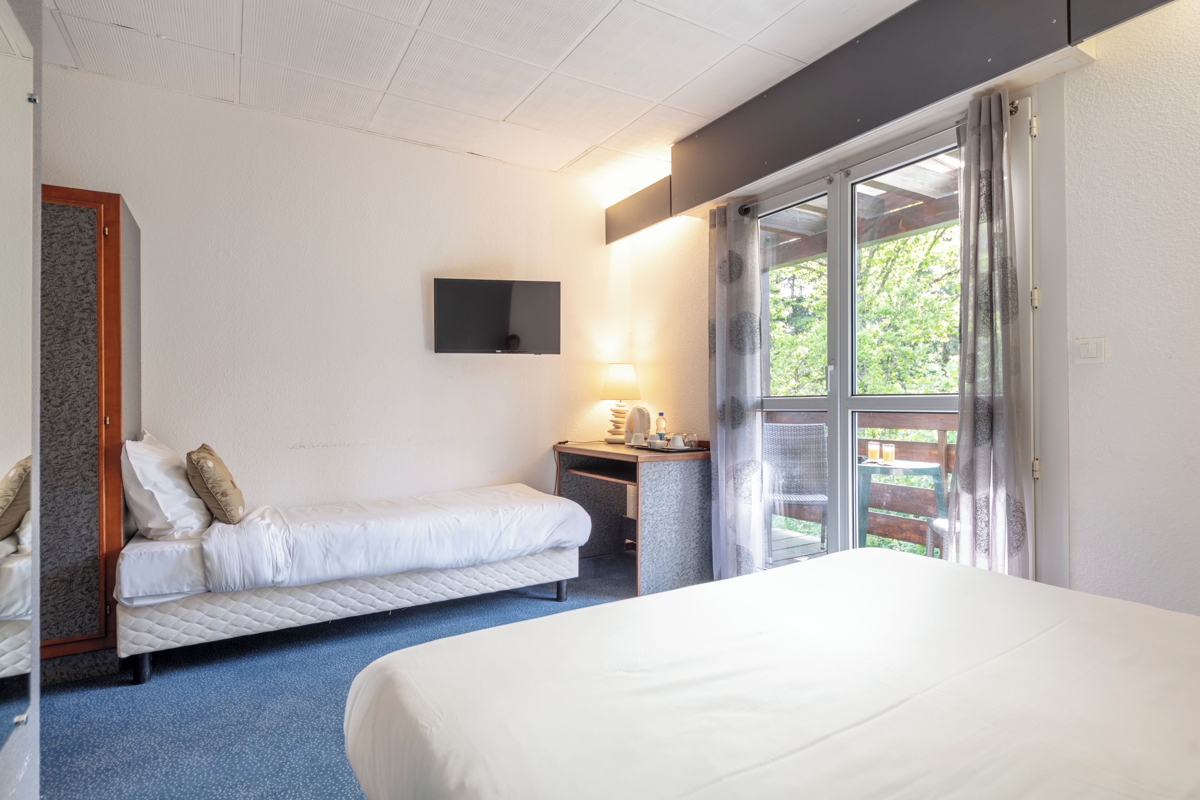 Hotelkamer met twee bedden, een bureau, een stoel, een televisie en een raam met uitzicht op groen.