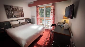 Ett hotellrum med en säng, ett skrivbord med en lampa, en tv och ett fönster med gardiner.