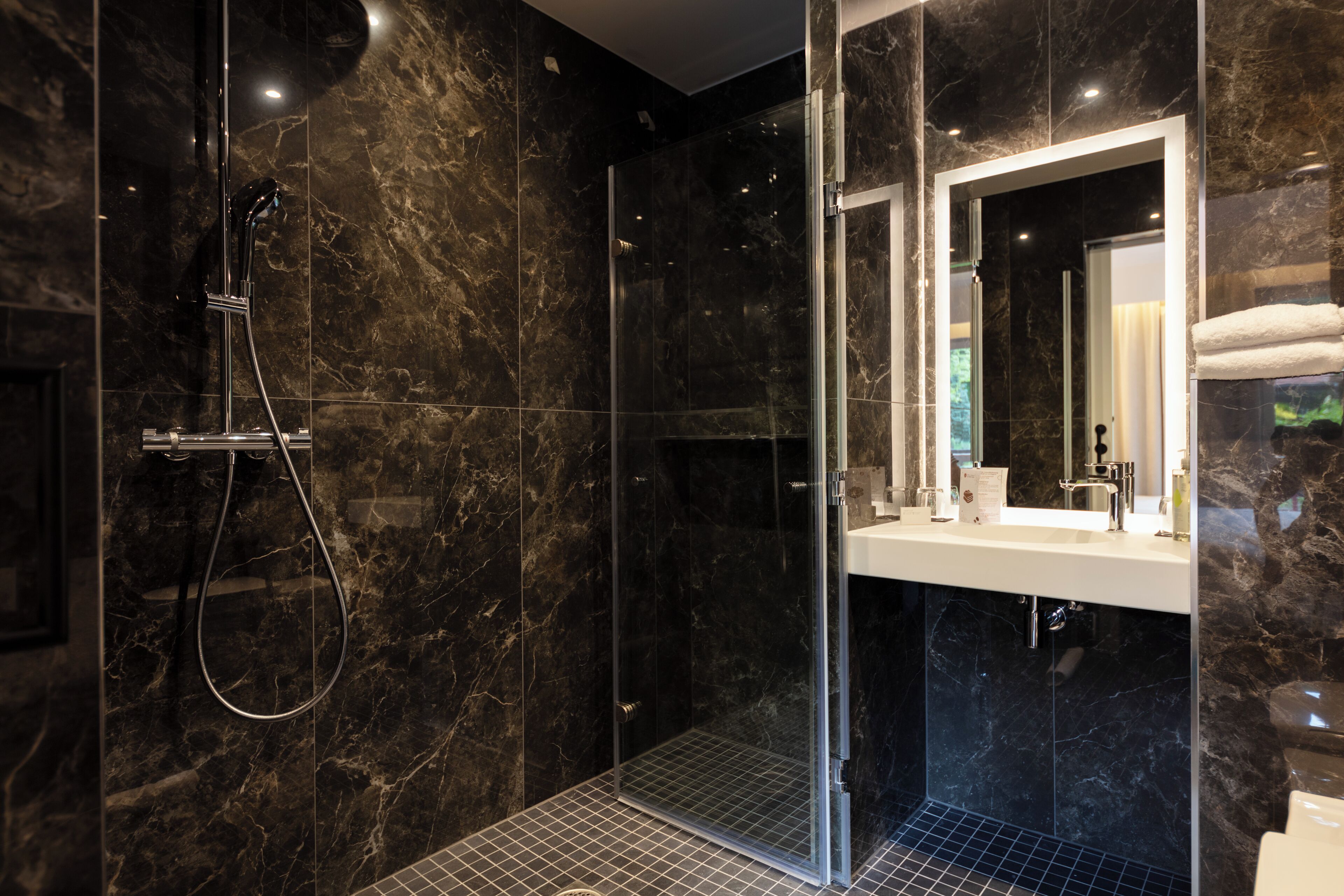 Een moderne badkamer met een douchecabine van glas, een grote spiegel en een witte wastafel.