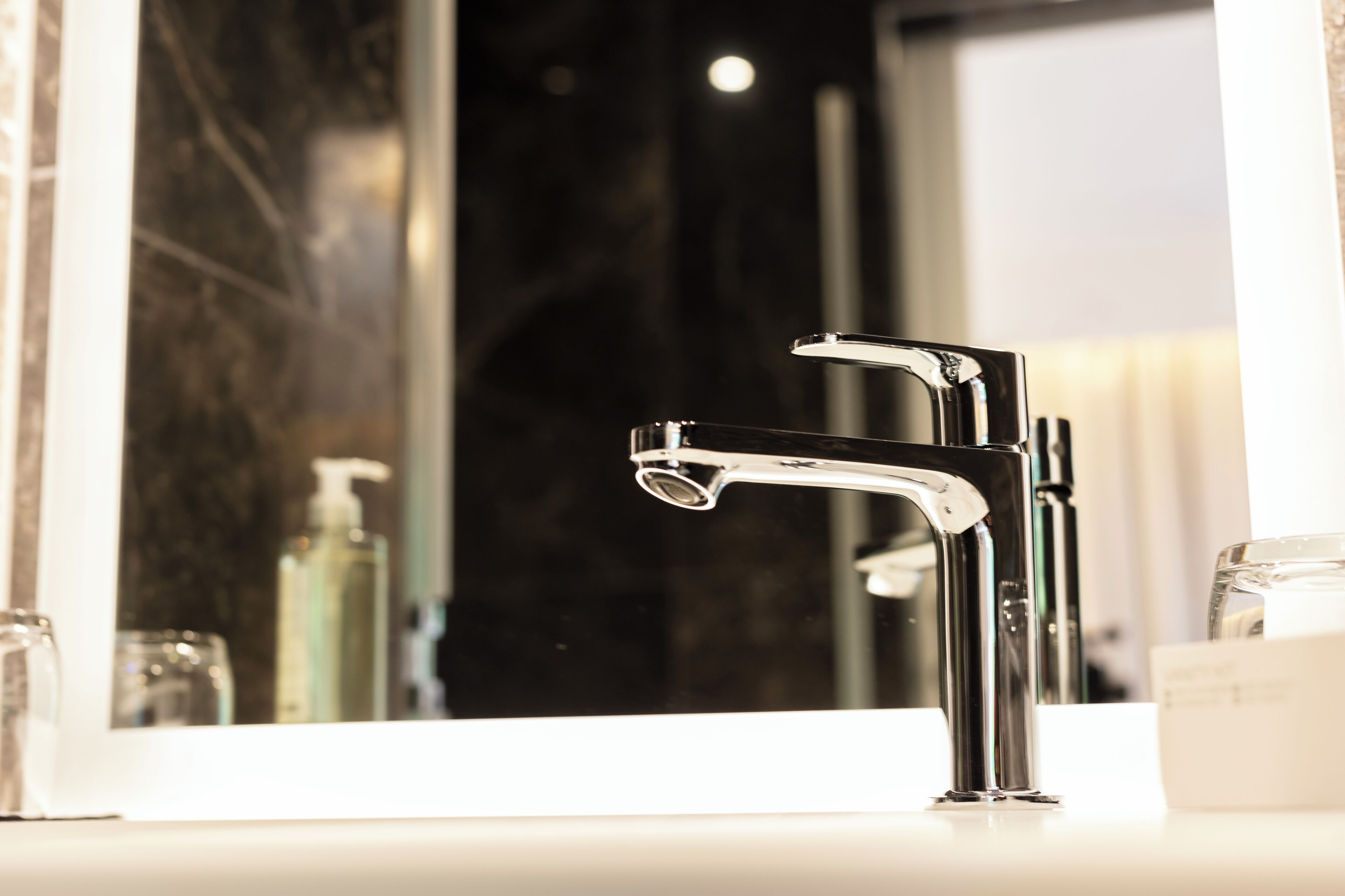 A modern bathroom with a chrome faucet, a mirror, and a white countertop.