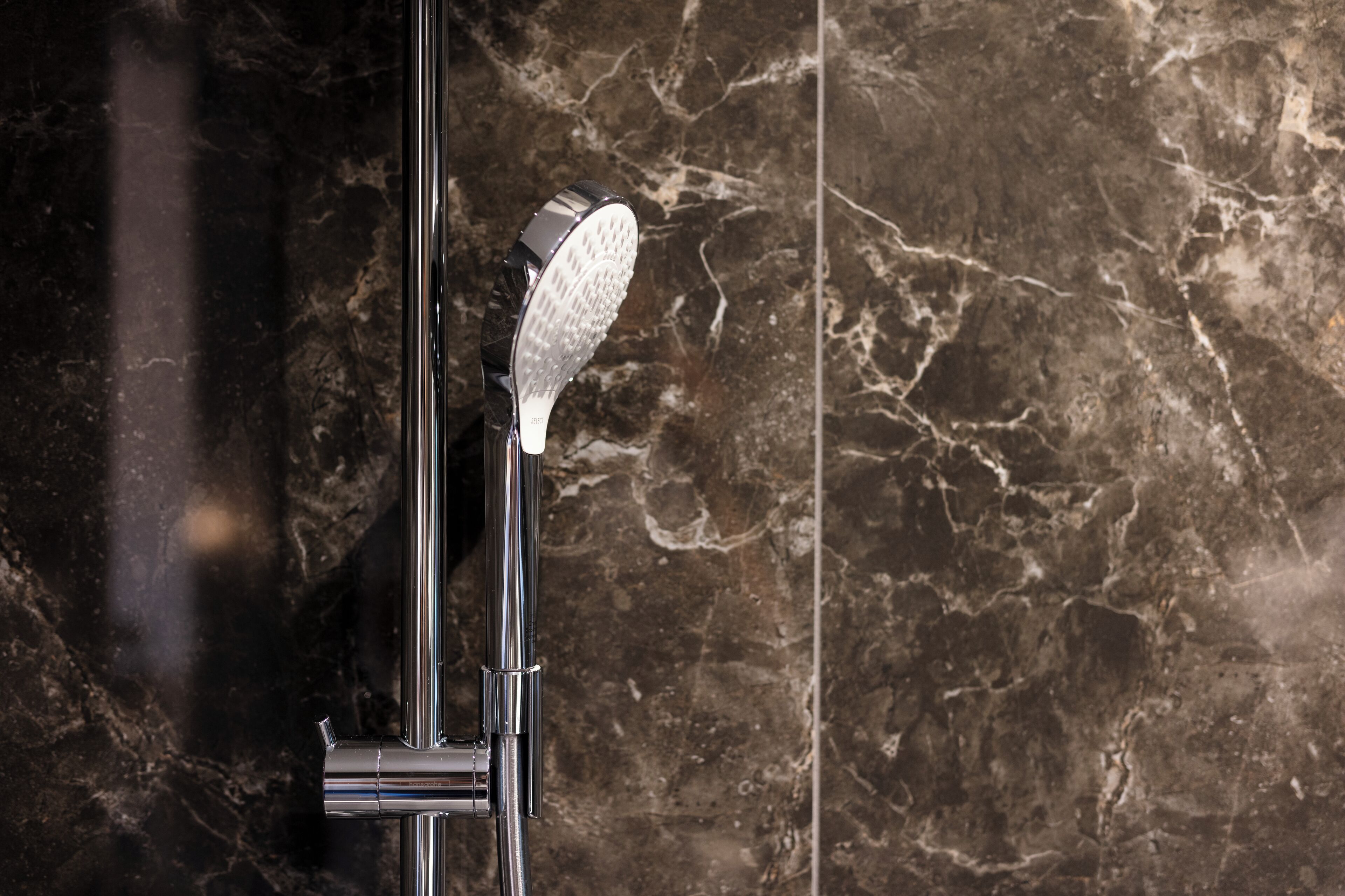 A modern shower with a handheld showerhead against a marble wall.