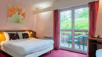 A hotel room with a bed, a painting of tulips, a window with curtains, and a view of greenery outside.