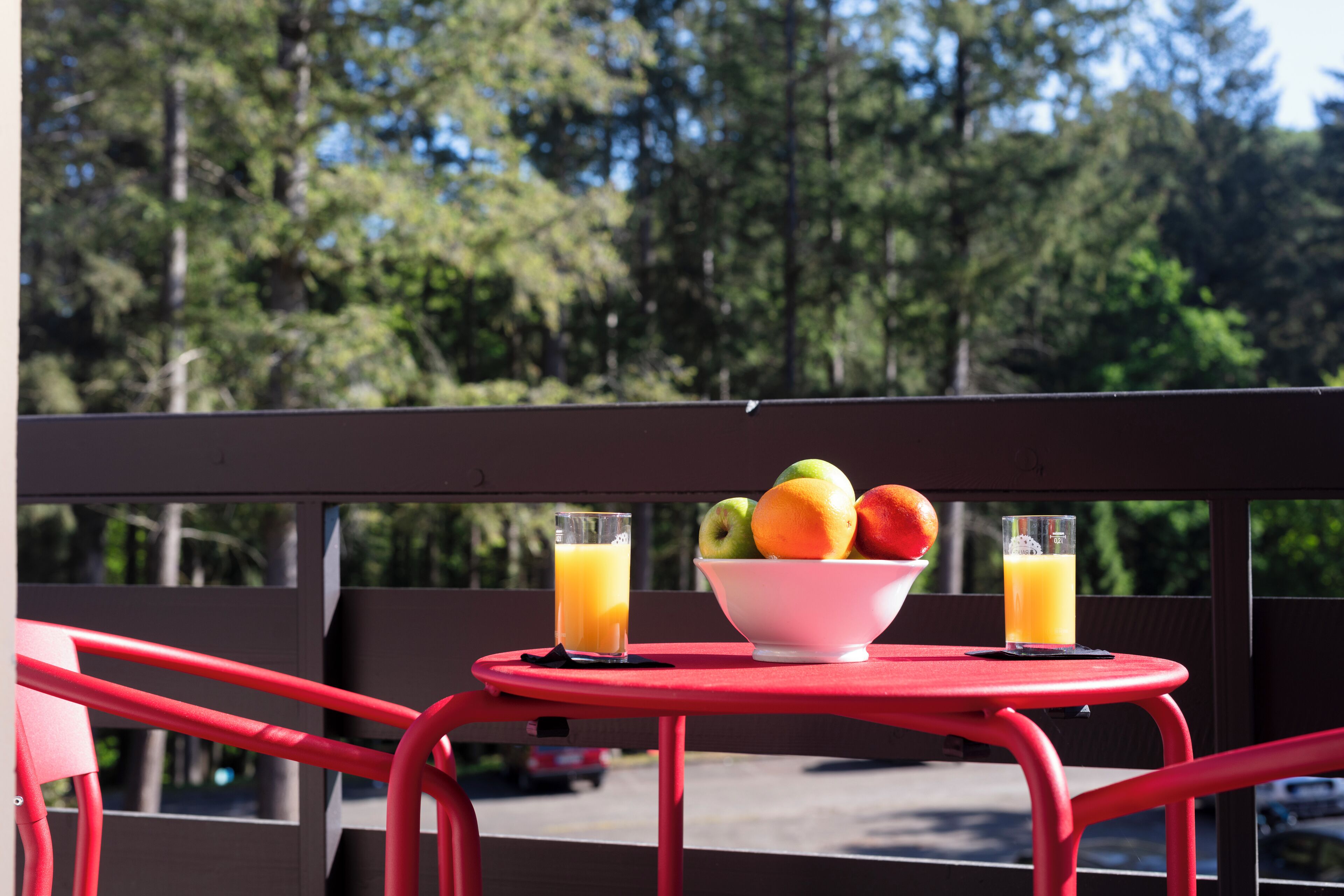 A red metal table with a bowl of fruit and two glasses of orange juice on a balcony.