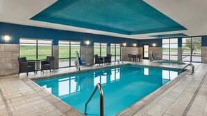 A swimming pool with a tiled deck, surrounded by chairs and tables, and large windows offering a view of the outdoors. - Hampton Inn Colby (Colby)