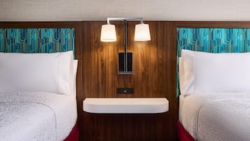 Habitación de hotel con dos camas, cabecera de madera, estante empotrado y lámpara fijada a la pared.