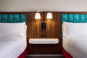 Ein Hotelzimmer mit zwei Betten, einem Holz-Kopfteil, einer fest installierten Ablage und einer Wandleuchte.