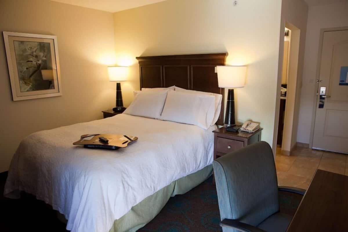 A hotel room with a bed, two bedside lamps, a desk with a telephone, a chair, and a door.