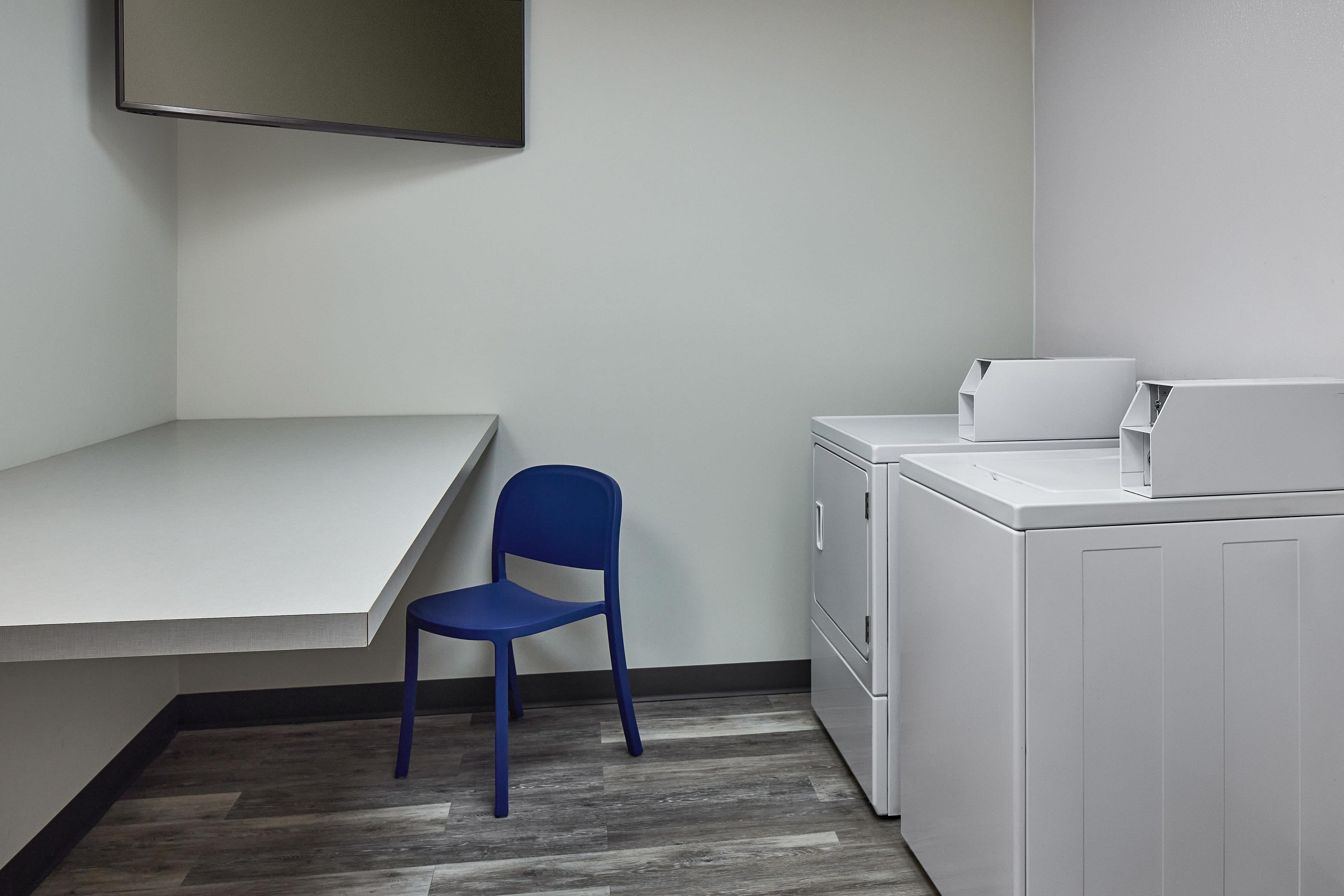 A laundry room with a washing machine, a chair, and a countertop.
