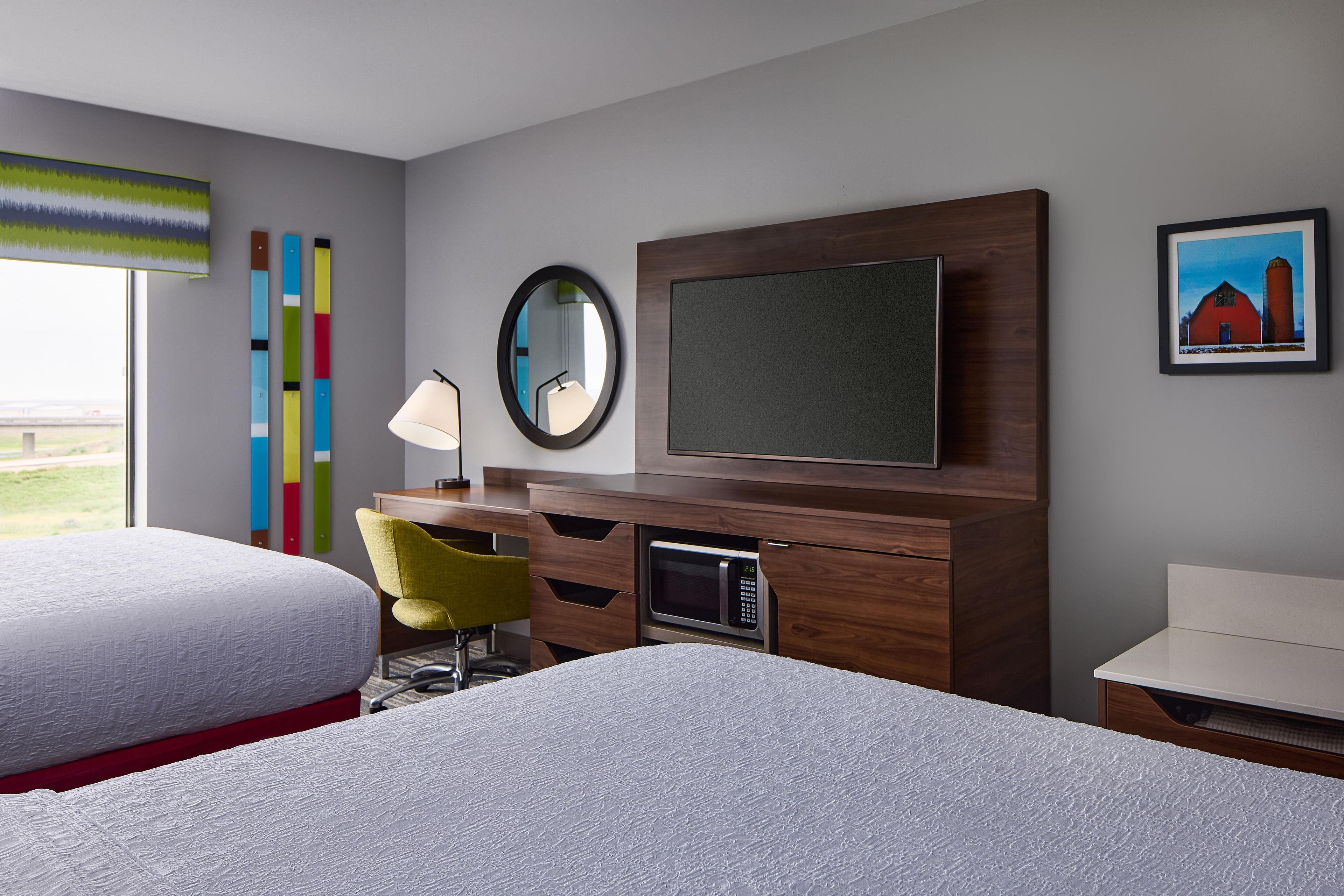 A hotel room with two beds, a desk, a TV, a mirror, and a painting.