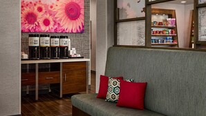 A modern interior with a sofa, a coffee station, and a wall with a sunflower painting. - Hampton Inn Colby (Colby)