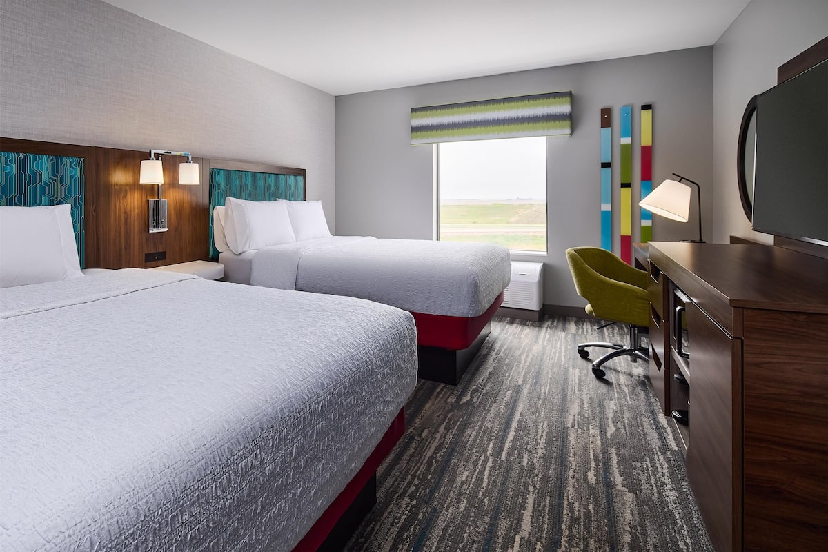 A hotel room with two beds, a desk, a chair, a TV, and a window with a view.