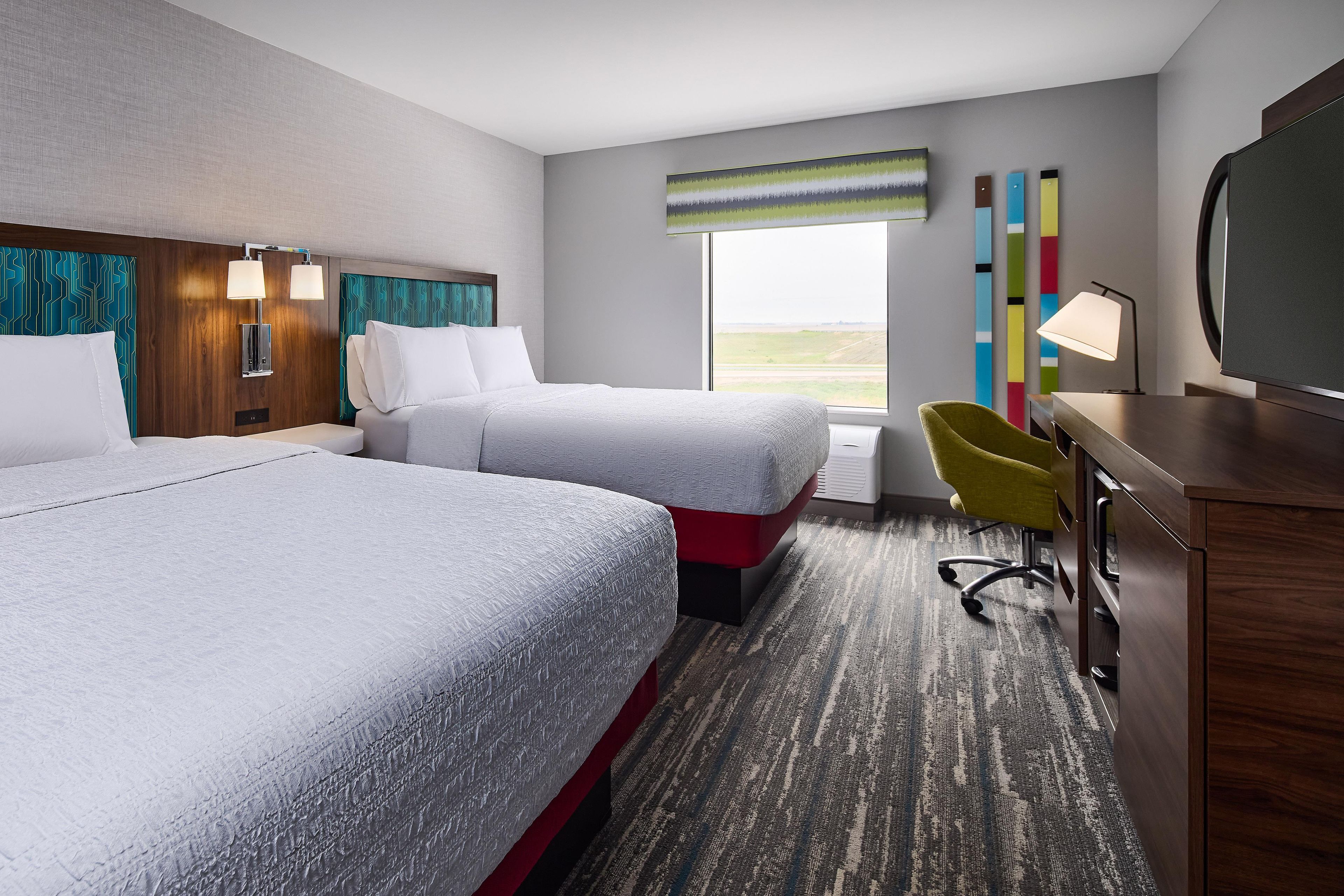A hotel room with two beds, a desk, a chair, and a large window.