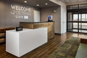 A reception desk with a 'Hilton Honors' sign, a clock, and a view of the parking lot through a glass door. - Hampton Inn Colby (Colby)